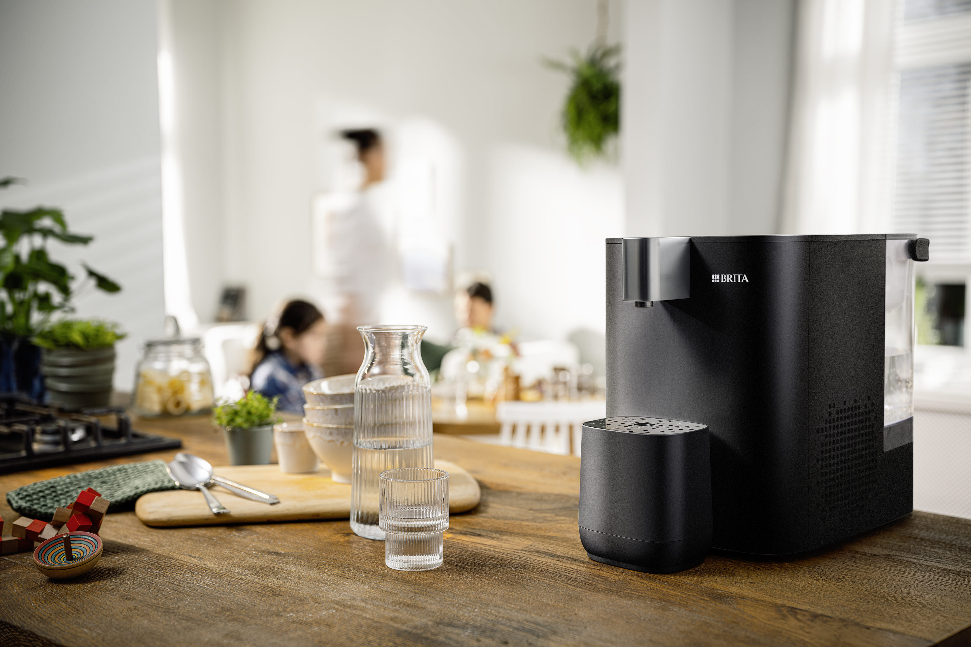 Schwarzer YOURCE cool Wasserspender mit Wasserglas auf einer Küchenarbeitsplatte 