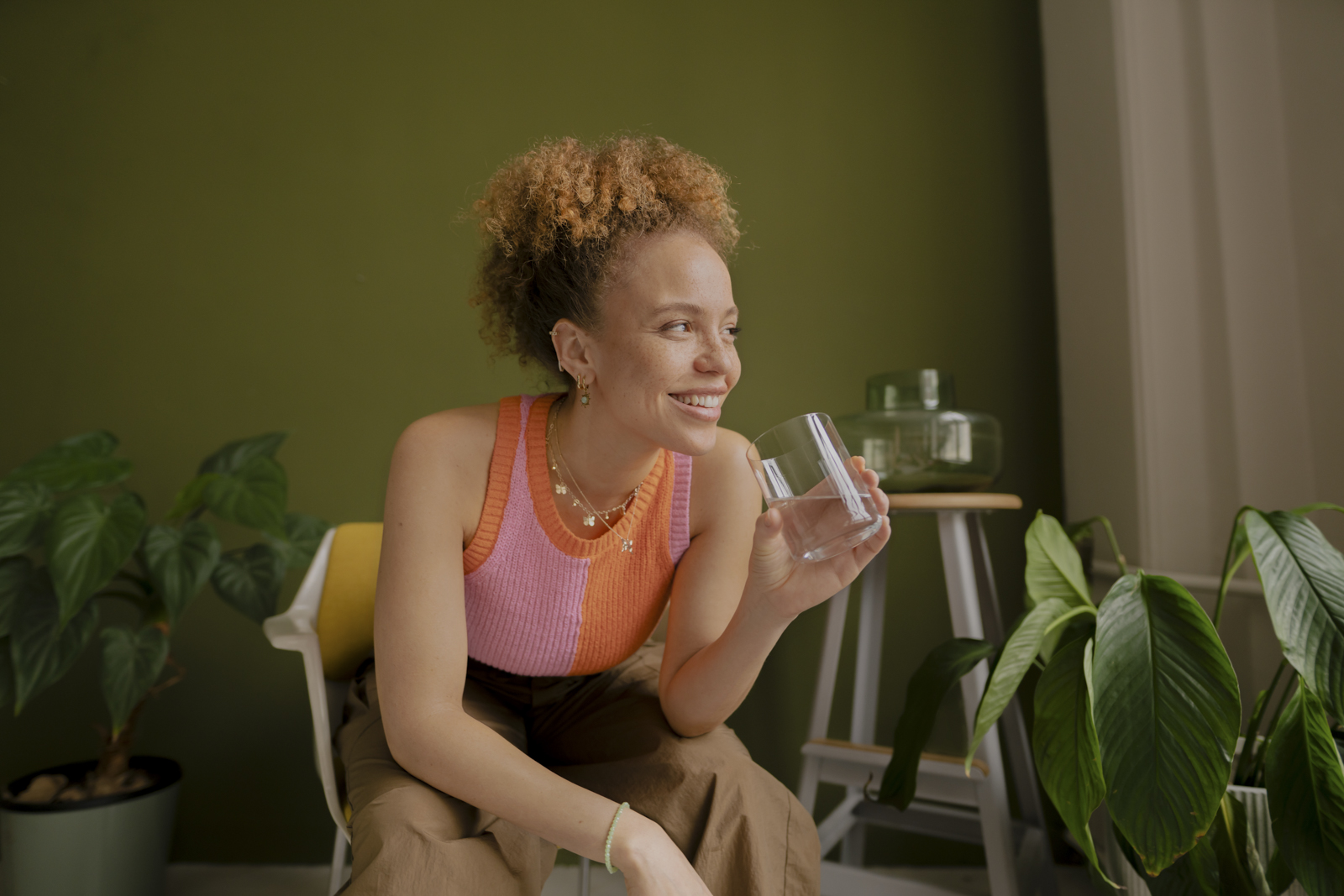 Frau hält lächelnd ein Glas Wasser Eine Frau sitzt lächelndauf einem Stuhl mit einem Glas Wasser in der Hand