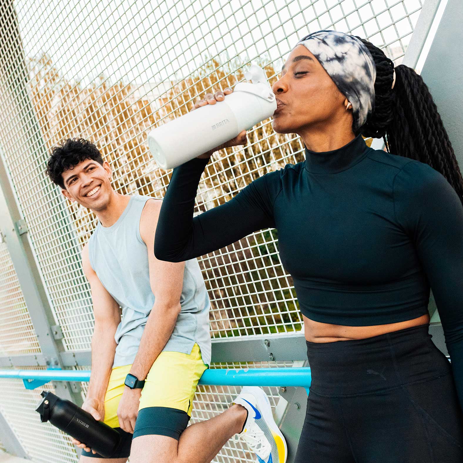 Mit der BRITA LARQ iQ beim Sport immer bestens hydriert Zwei sportliche Personen machen eine Pause im Freien – eine trinkt aus einer weißen BRITA LARQ iQ Fi