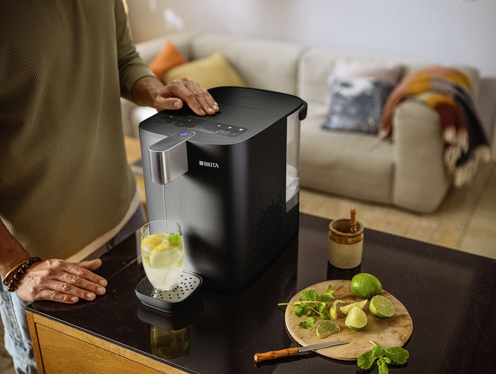 Der YOURCE cool Wasserspender mit kaltem Wasserglas und Zitronnen, platziert in einem Wohnzimmer