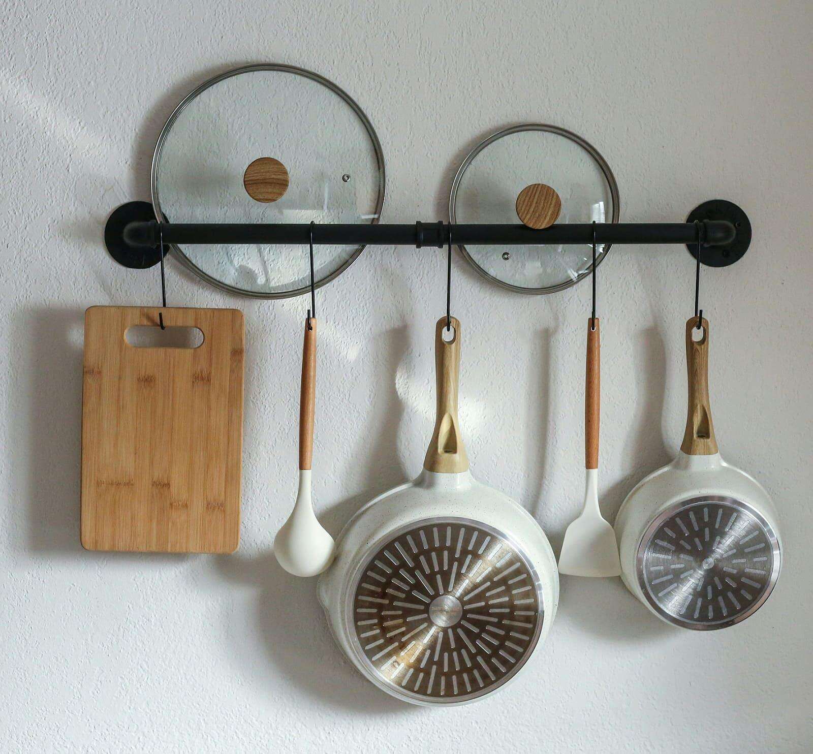 Pfannen und Kochlöffel an einer weißen Wand Pfannen und Kochlöffel an einer weißen Wand