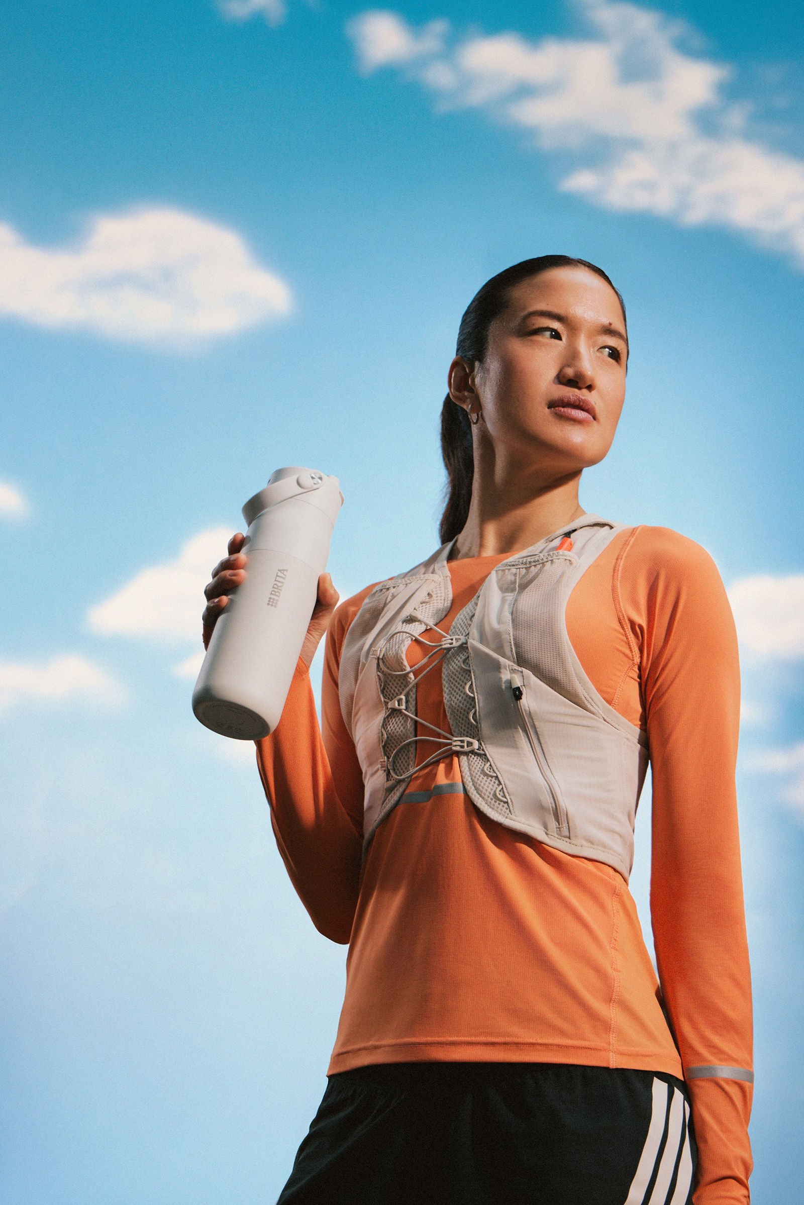Läuferin in Sportkleidung hält eine Trinkflasche in der Hand Läuferin in Sportkleidung hält eine Trinkflasche in der Hand, vor blauem Himmel