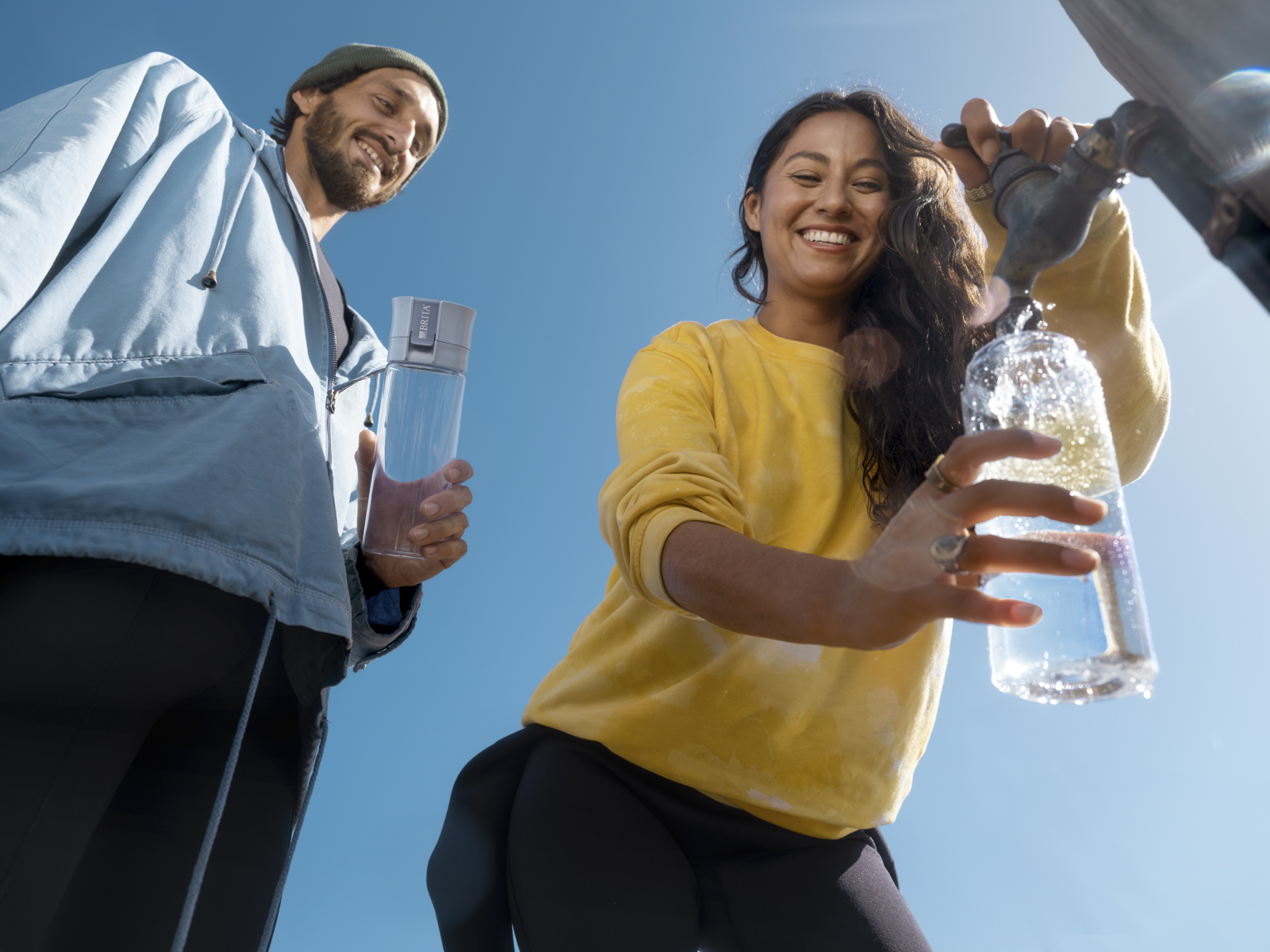Frau füllt draußen eine Trinkflasche mit Filter Frau füllt draußen an einem öffentlichen Wasserhahn eine BRITA Trinkflasche mit Filter