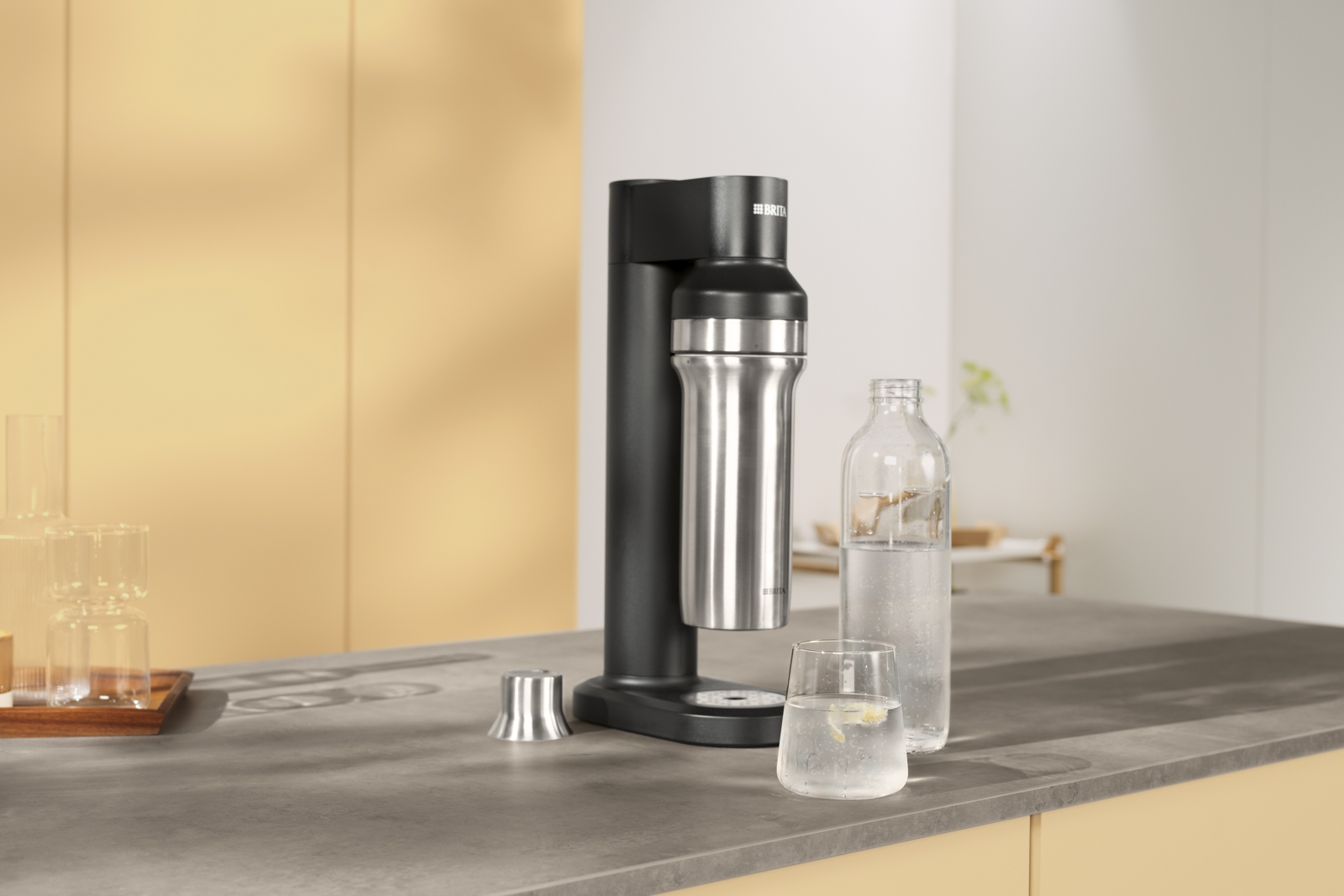 Wasser steht vor dem BRITA sodaTRIO Eine Flasche und ein Glas Wasser stehen vor dem schwarzen sodaTRIO