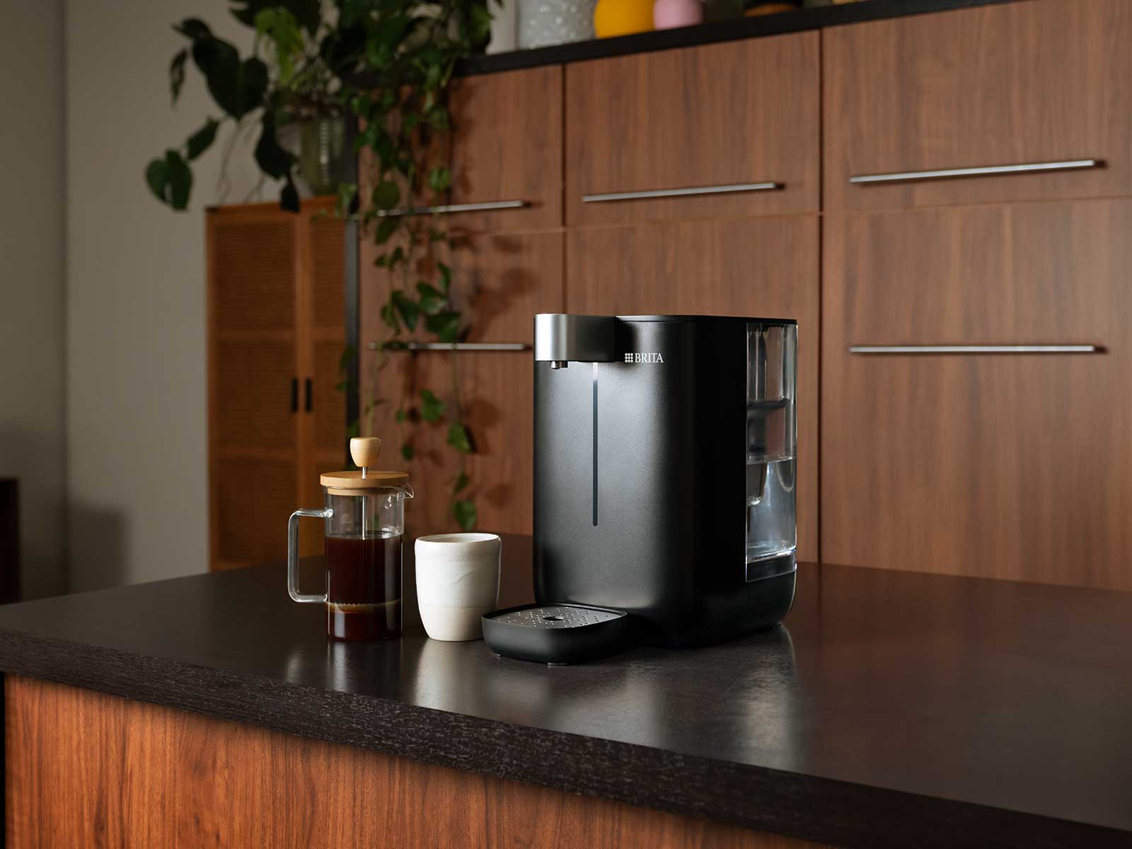 BRITA Cube mit Kaffee und Tasse Ein schwarzer BRITA Cube steht neben einer weißen Tasse und einer Kaffeefilterkanne auf der Küchenth