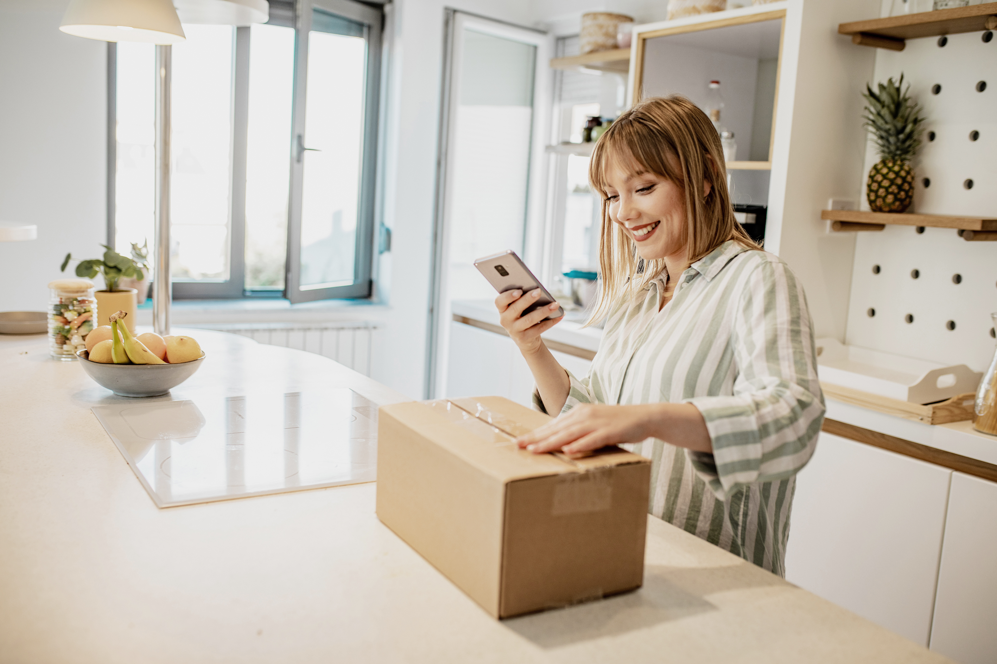 Eine Frau steht in der Küche und öffnet mit Vorfreude ein Paket