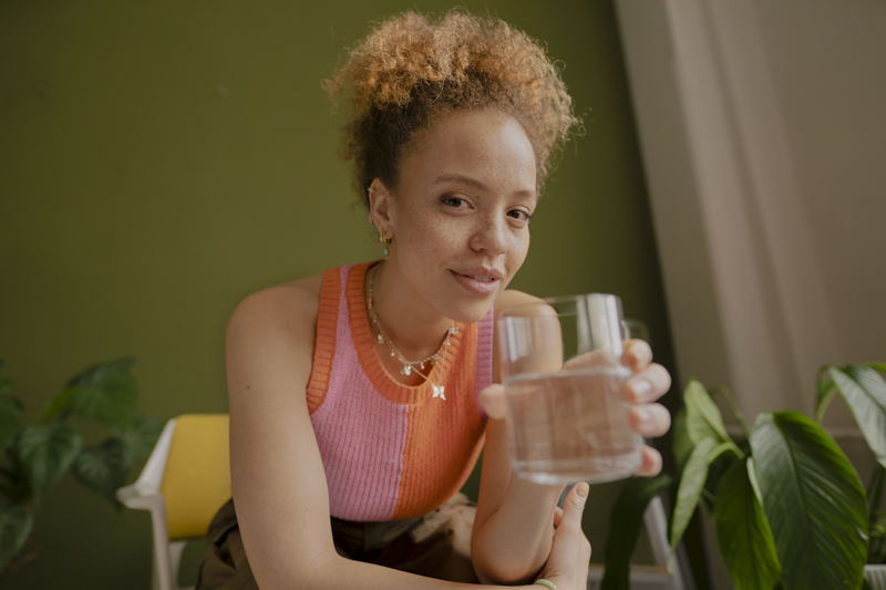 Frau in pink-orangem Top hält ein Glas BRITA gefiltertes Wasser