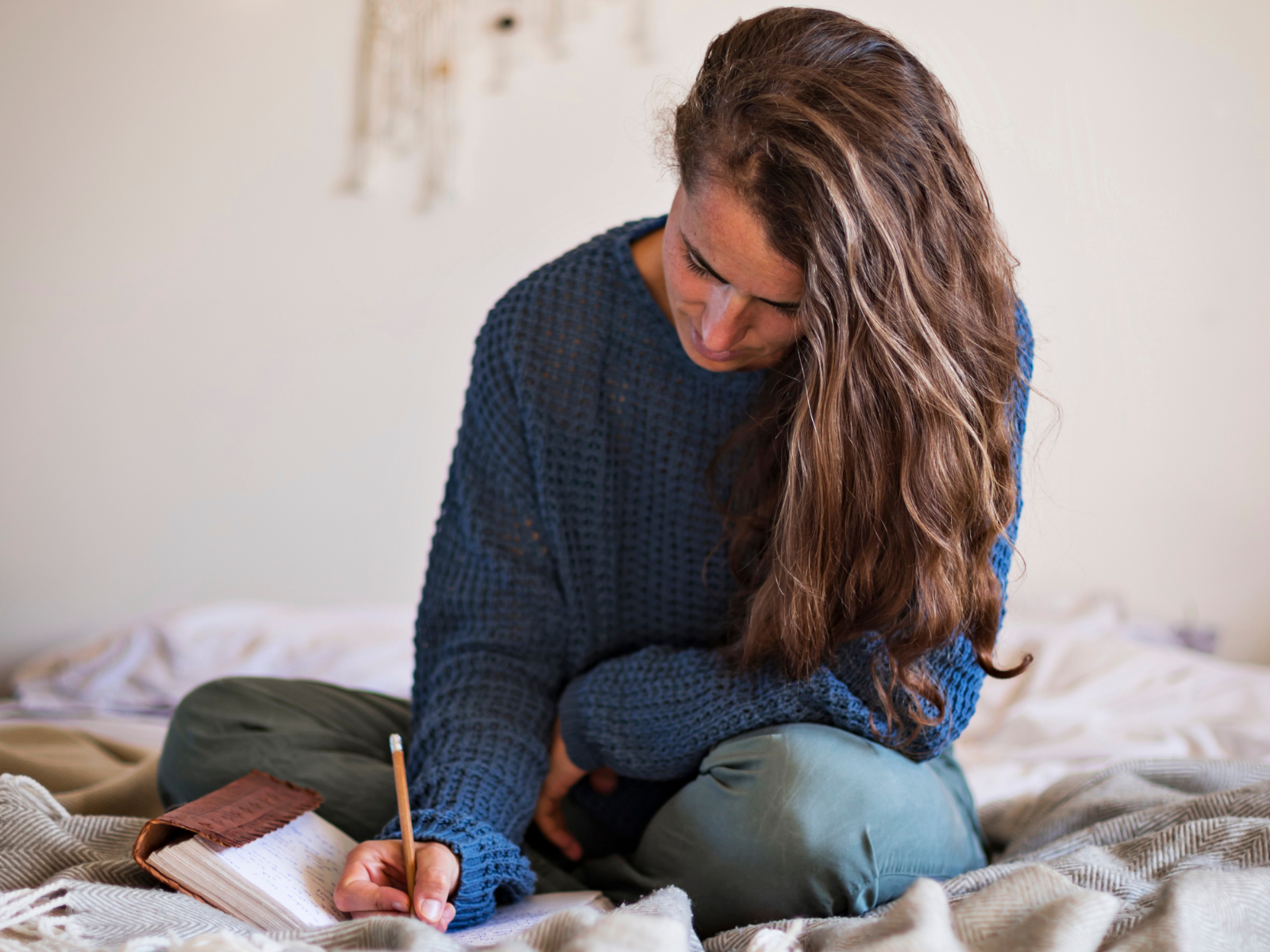 Frau sitzt auf dem Bett und notiert ihre Gedanken in ein Notizbuch.