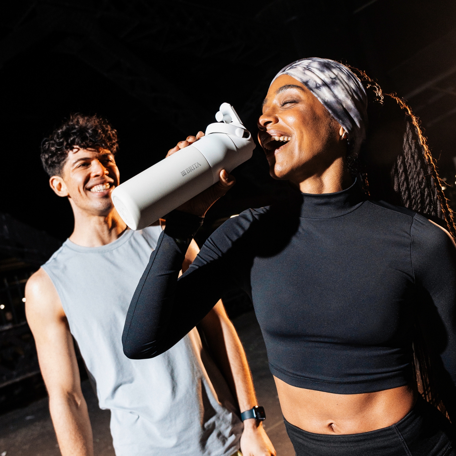 Junge, glückliche Menschen mit weißer BRITA LARQ Flasche Ein junger Mann trinkt an einer BRITA LARQ Flasche, daneben ein junger, lächelnder Mann