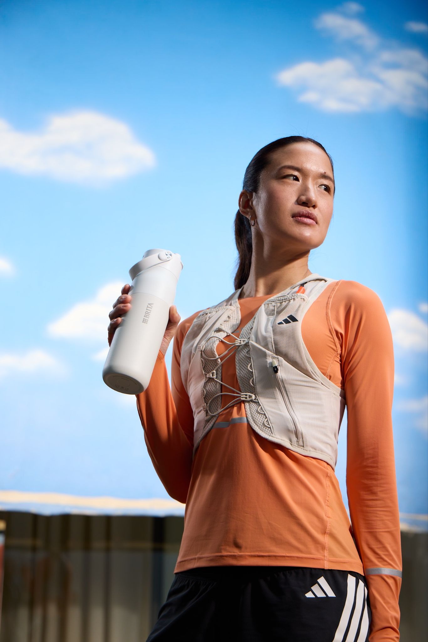 Läuferin hält eine weiße BRITA‑Trinkflasche Sportlich gekleidete Läuferin hält eine weiße BRITA‑Trinkflasche vor blauem Himmel.