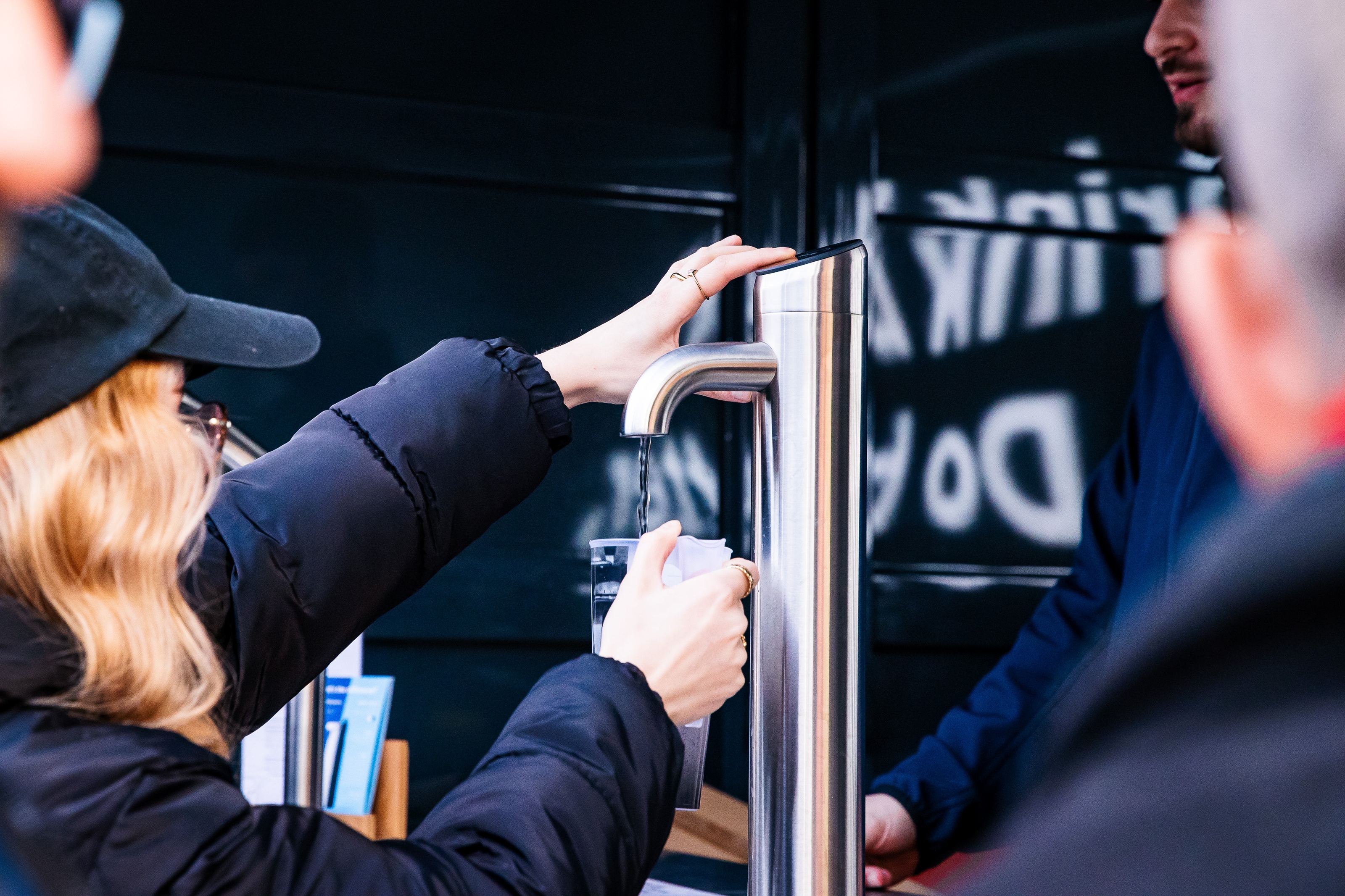 Personen zapfen Trinkwasser an mobiler Edelstahl-Wasserstation im Außeneinsatz.<br/>