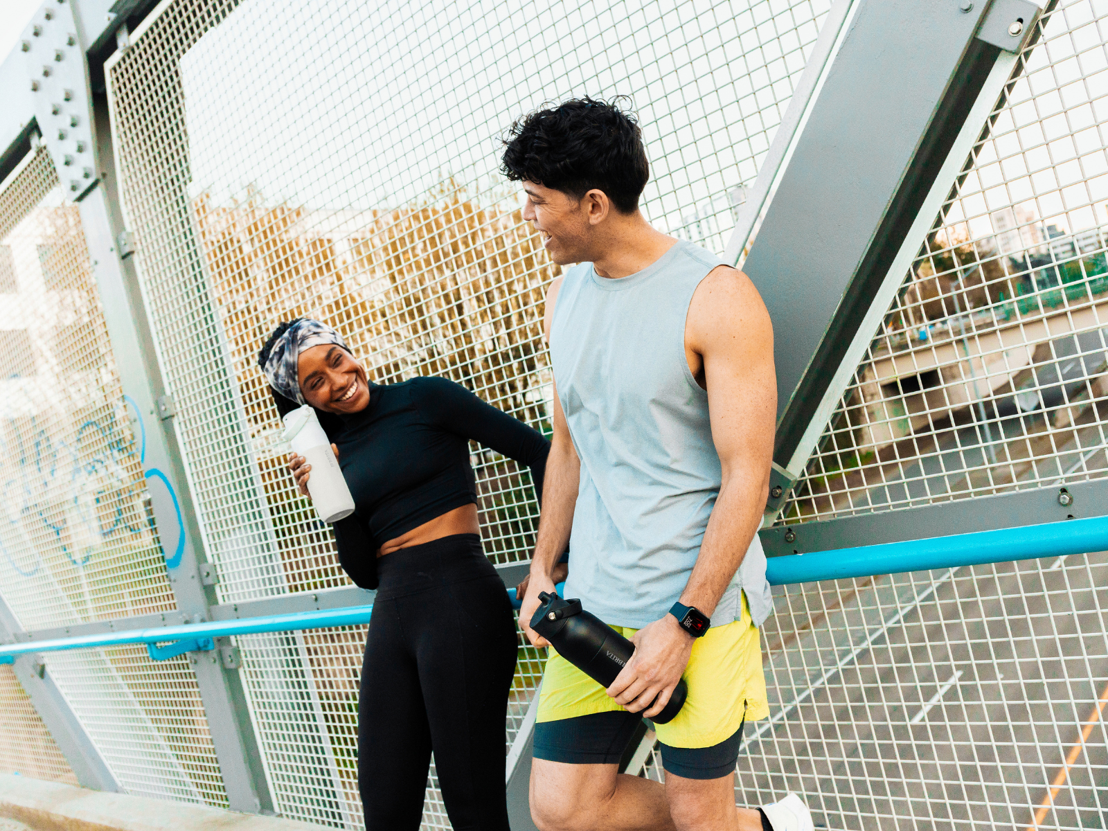 Wasser als Energiebooster Zwei Sportler:innen lehnen an einer Brücke und halten ihre BRITA LARQ iQ Wasserfilterflasche.