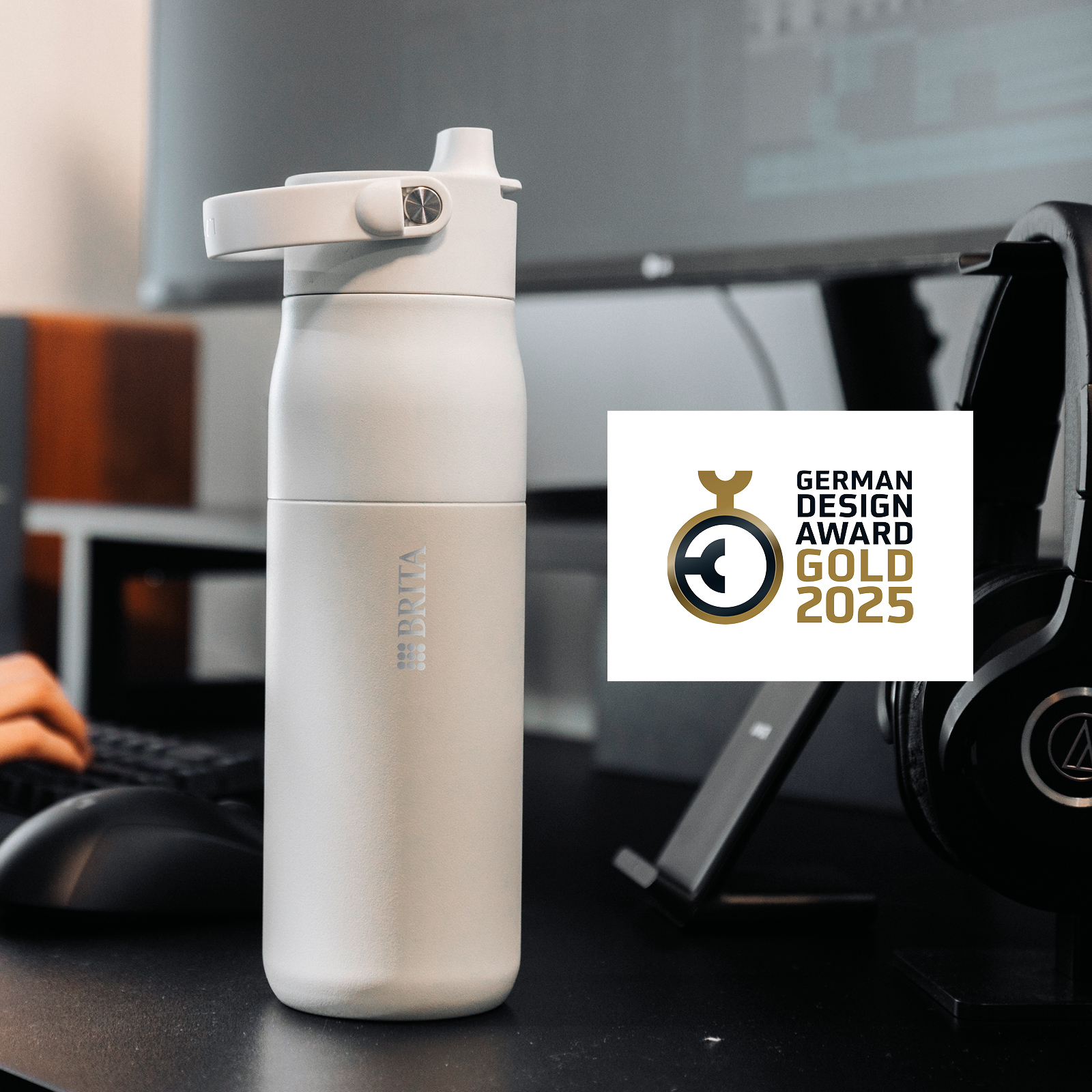 BRITA LARQ IQ im Büro mit dem Design Award Logo Eine weiße BRITA LARQ IQ steht auf einem Schreibtisch, daneben ist das Design Award Logo abgebildet