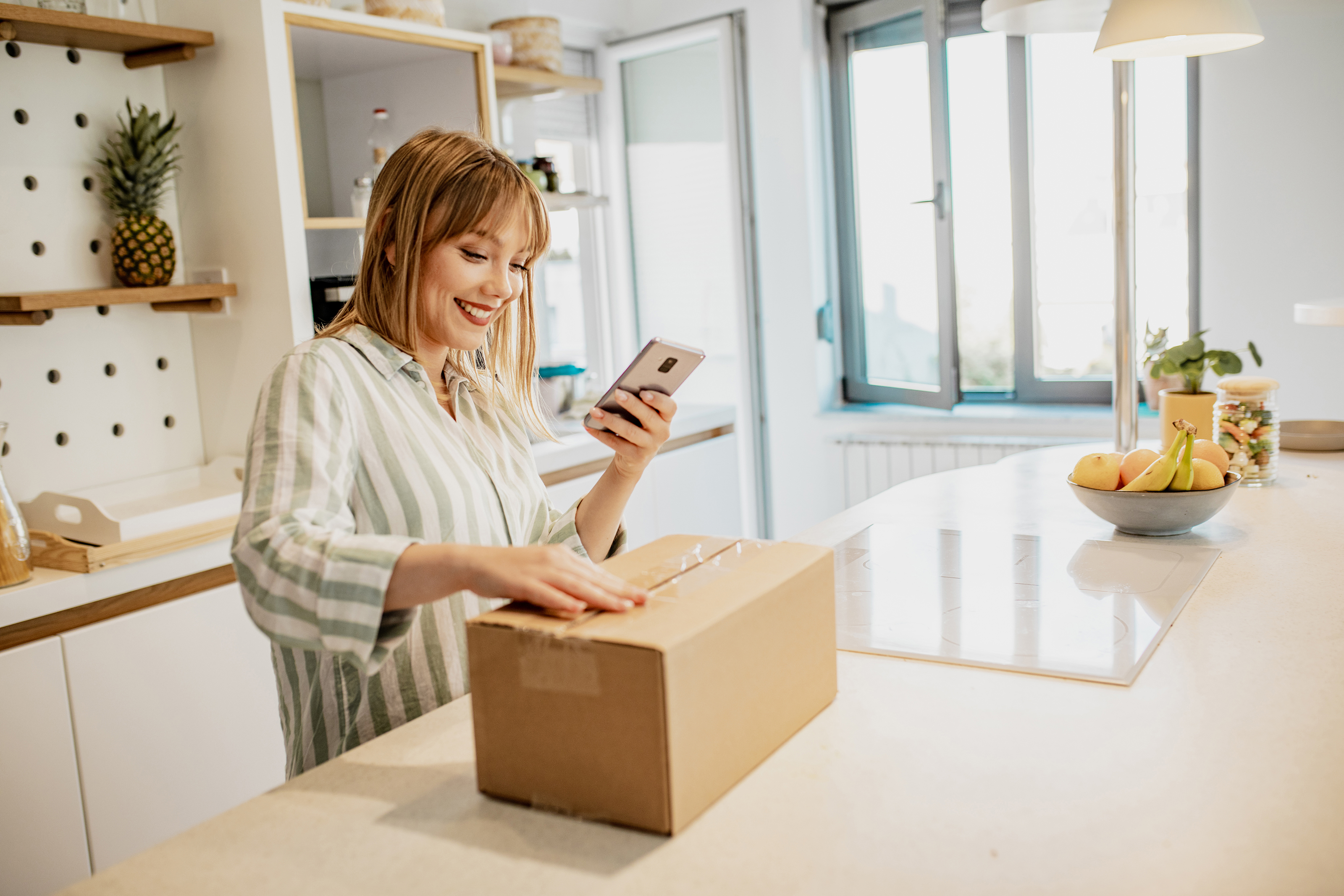 Eine Frau steht in der Küche und öffnet mit Vorfreude ein Paket