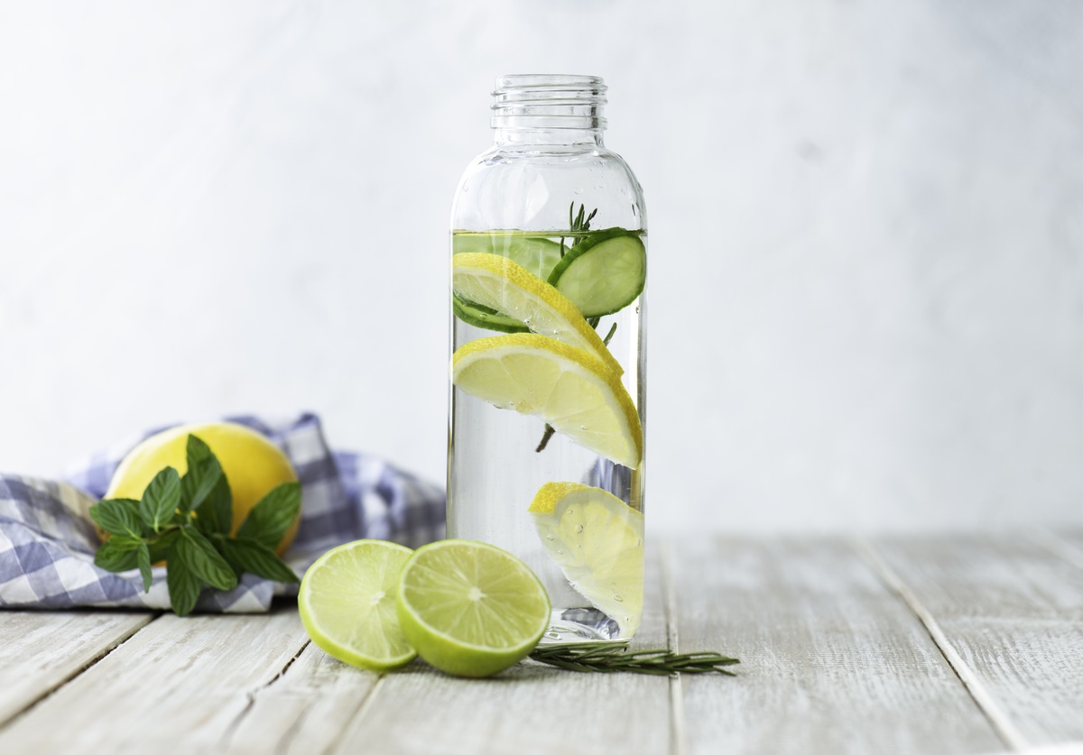 Glasgefäß mit von BRITA gefiltertem Wasser, Minze, Gurken- und Zitronenscheiben auf einem Holztisch