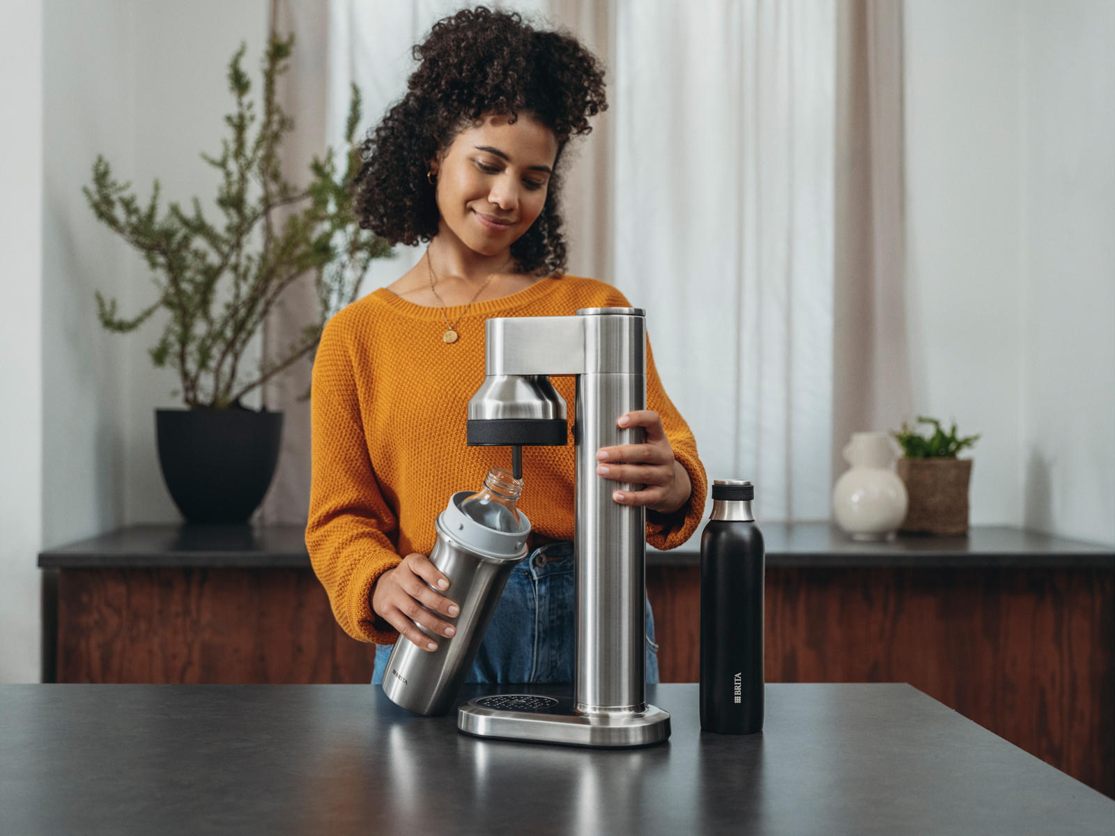 Eine Frau schraubt eine Flasche in den BRITA sodaTRIO pro Wassersprudler.