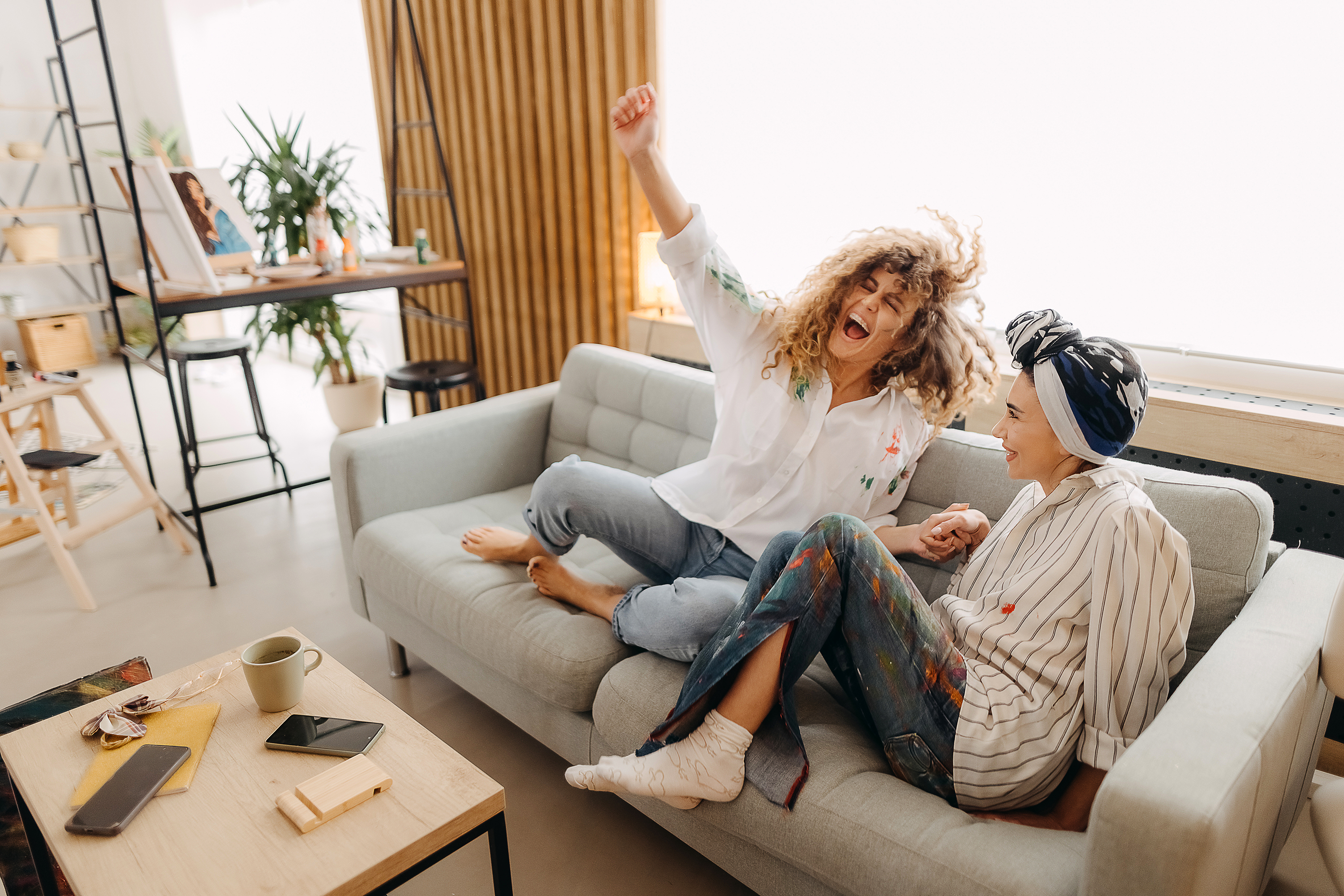 Zwei junge Frauen sitzen glücklich auf der Couch Zwei junge Frauen feiern sitzend auf der Couch das Leben