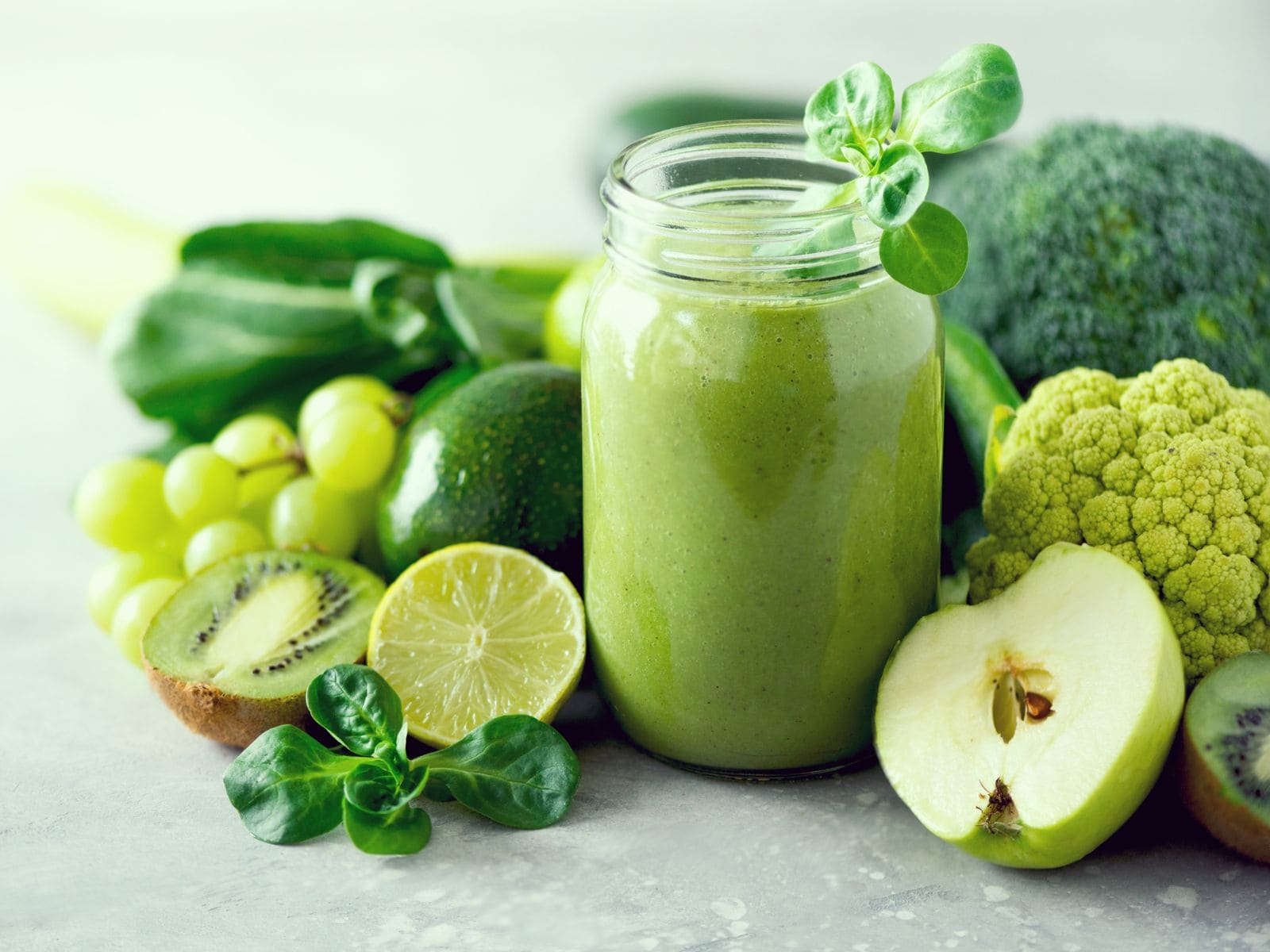 Grüner Smoothie in Glas mit nebenliegenden grünen Früchten Grüner Smoothie in Glas mit nebenliegenden grünen Früchten