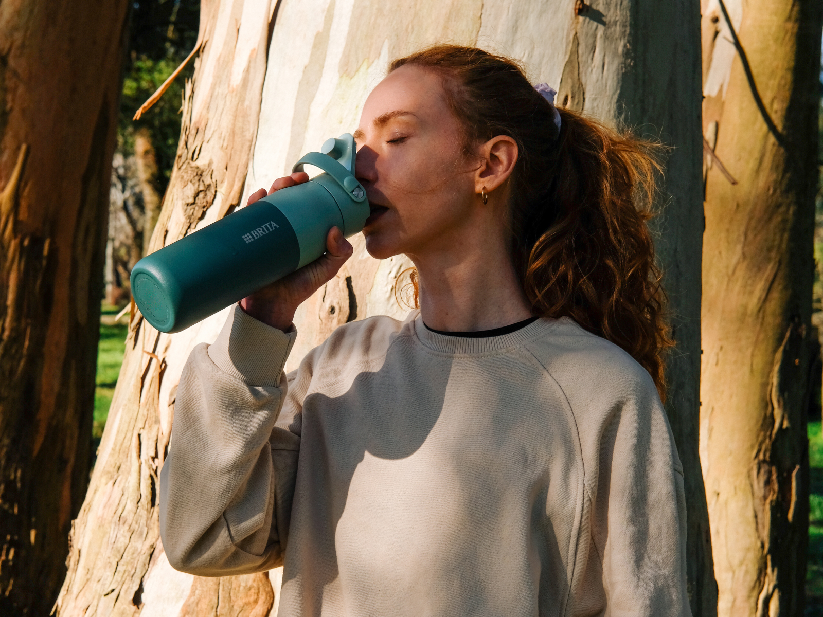 Frau ist in der Natur unterwegs und trinkt aus der BRITA LARQ Essential Trinkflasche mit Filter.