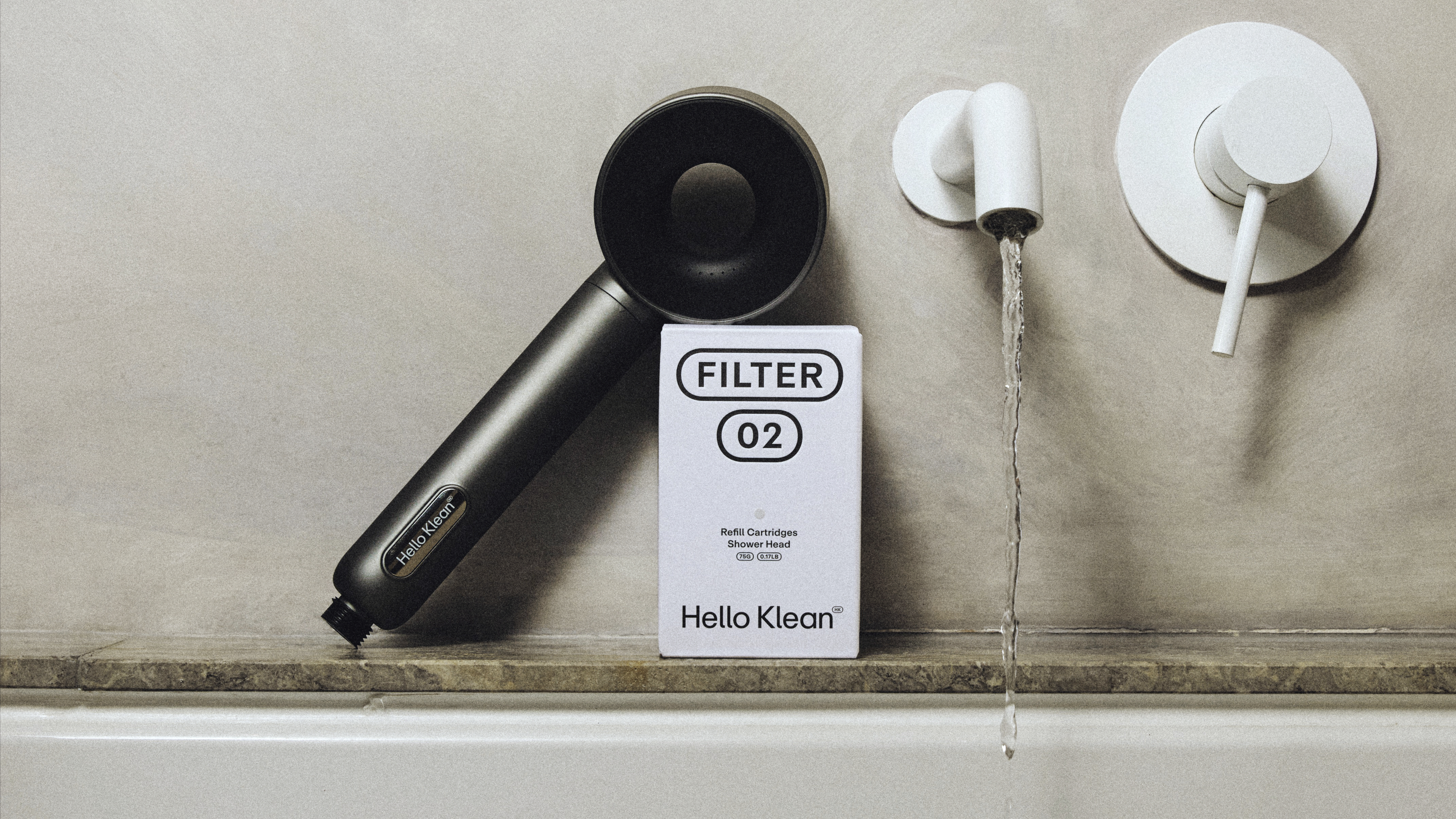 Hello‑Klean‑Duschkopf mit Filter neben der Produktverpackung Hello‑Klean‑Duschkopf mit Filter 02 neben der Produktverpackung, Wasser fließt aus der Armatur.